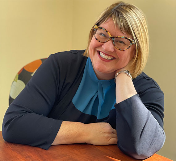 Un grupo de cinco personas está reunido en un pasillo de hospital bien iluminado, sonriendo a la cámara. Dos llevan estetoscopios y ropa médica, uno lleva una sudadera de la Universidad Gonzaga, y los demás visten ropa casual o profesional, representando una mezcla de estudiantes y profesionales de la salud.